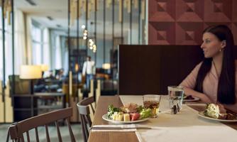An elegant restaurant with a table on which a beautifully arranged plate of food is placed. In the background, a woman can be seen sitting in a relaxed atmosphere.