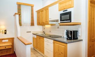 A modern kitchen with wooden cabinets and light walls. It is fully equipped with a stove, microwave, and coffee maker.