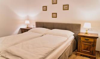 A cozy bedroom with a double bed and stylish bedside tables. The walls are decorated with small pictures, and warm light from the lamps creates an inviting atmosphere.