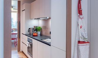 A modern kitchen with bright cabinets and a black work area. In the background, a dining area with red chairs is visible.