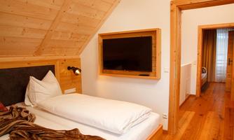 A cozy bedroom with wooden paneling and a large window. There is a bed with pillows and a wall with a television.