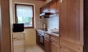 A small kitchen with wooden cabinets and bright tiles. The window lets in natural light and offers a view outside.