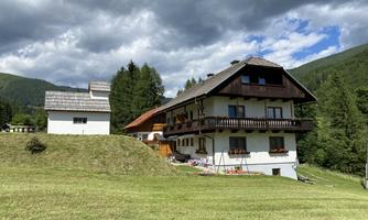 A picturesque house in the mountains with a large garden. The sky is covered with clouds and the landscape is green.