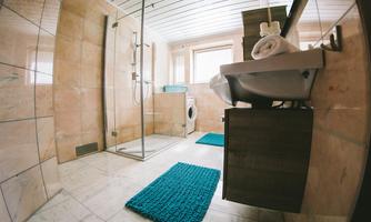 A modern bathroom with a shower and a sink. The floor is equipped with elegant tiles and blue bath mats.