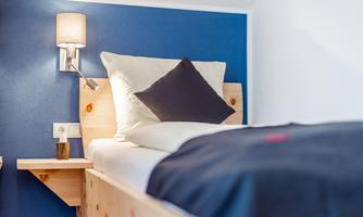 A modern bedroom with a cozy bed and a blue wall. There is a bedside lamp and pillows on the bed.