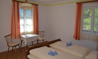A simple room with two single beds, a table, and two chairs. Bright curtains and a window create a friendly atmosphere.