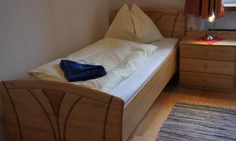 A simple bedroom with a single bed and a bedside table. The room decoration is simple and modern, featuring a rug and windows with curtains.