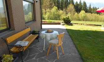 A cozy terrace with a bench and a table. In the background, trees and green countryside can be seen.