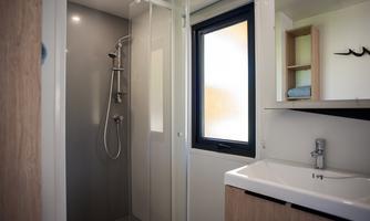 A modern bathroom with a shower cubicle and a hand wash basin. The design is sleek and elegant, featuring wood and gray tones.
