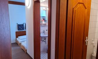 A well-lit hallway with access to a bathroom and a bedroom. The walls are light, and the furniture is made of light wood.