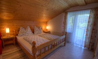 A cozy bedroom with a wooden ceiling and a double bed. There are two nightstands and a balcony that lets in plenty of light.