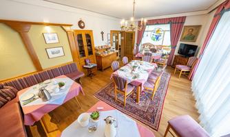 An inviting dining room with tables set for a meal. Bright colors and a window with stained glass create a friendly atmosphere.