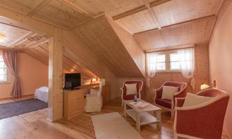 A cozy room in the attic with wooden paneling. Two red-and-white armchairs and a small table complete the furnishings.
