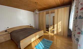 A bright bedroom with a wooden ceiling and a large bed. A carpet and a mirror wardrobe complete the furnishings.
