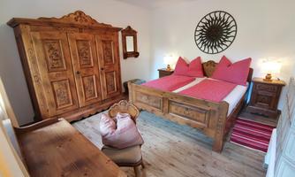A cozy bedroom with a wooden wardrobe, a double bed, and harmonious furniture. The decorative studs and the decorative cushions give the room an inviting atmosphere.
