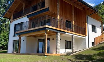 A modern house with wooden cladding and several balconies.  
Surrounded by green spaces and under a clear blue sky.