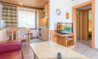 A bright and friendly apartment with a living area, a kitchen, and a dining area. In the background, a bedroom is visible.