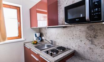A modern kitchen with red cabinets and a stone countertop. There is a sink, a kettle, and a microwave.