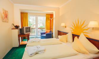 A bright room with two beds and yellow pillows. The room has a balcony and a television.