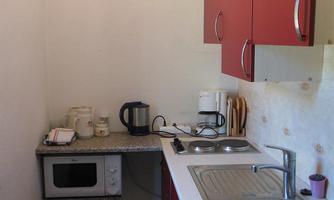 A small kitchen with red cabinets and modern appliances. It includes a sink, a microwave, and a kettle.