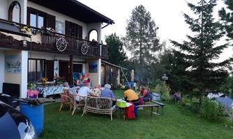 A relaxed group is sitting outside at a table in front of a beautiful house. Surrounded by trees and a green garden, they are enjoying their time together.