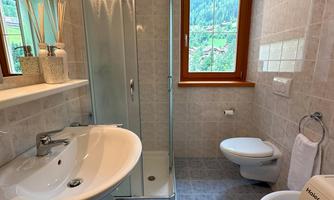 A modern bathroom with a shower, sink, and toilet. It has a window that offers a view of nature.