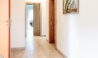 A bright hallway with an orange door and an artistic picture on the wall. The floors are tiled and wooden.