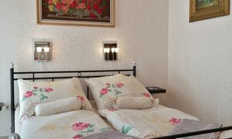 English
Black metal double bed with two separate duvets featuring a rose motif and folded grey textiles at the foot; two wall lamps and two framed pictures.