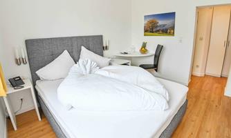 A cozy bedroom with a large bed and a gray headboard. There is a table, a chair, and a window with curtains.