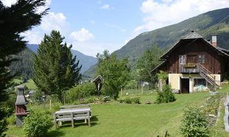 An idyllic garden estate with a traditional wooden house and a beautiful meadow. In the background, green mountains and a blue sky can be seen.