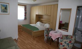 A cozy room with a double bed and wooden furniture. A small sitting area with a table and chairs completes the space.