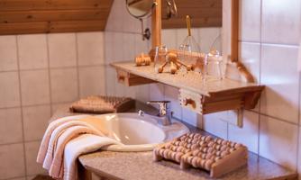 A modern bathroom with an elegant sink and wooden shelves. Towels and various utensils are placed on the shelf.
