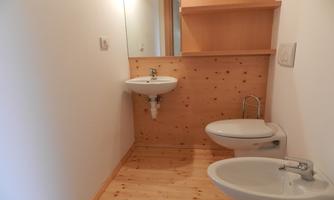A modern bathroom with wooden paneling. It features a sink and a toilet, as well as a bright, friendly atmosphere.