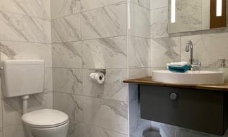 A modern bathroom with marble tiles. There is a toilet, a sink, and a mirror.
