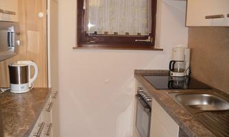 A small, modern kitchen with bright furniture. It has a stove, a sink, and a window with a curtain.