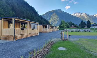 Modern wooden cabins set against a picturesque mountain backdrop. The surroundings are calm and natural, perfect for a stay in nature.