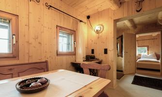 A cozy room with wooden paneling and a table. In the background, a bedroom is visible.