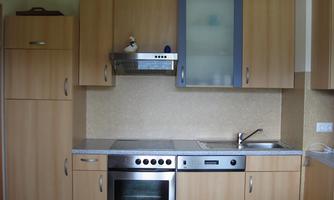 A modern kitchen with wood cabinets and stainless steel appliances. The countertop is made of gray material and the wall is bright.