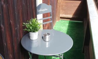 A small balcony with a round table and two chairs. On the table, there is a flower pot and a candle.