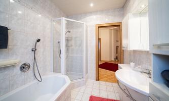 A modern bathroom with a shower and a bathtub. The walls are light tiled, and a washbasin is present.