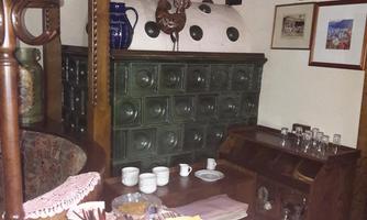 A cozy room with a table set with dishes and kitchen utensils. In the background, there is a decorative oven and several pictures on the wall.