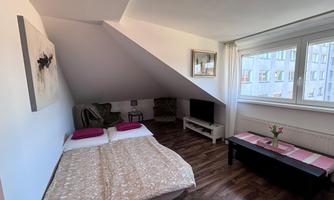 A cozy room with two beds and a television. Large windows let in a lot of daylight and offer a view of city life.