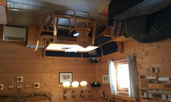 A cozy living room with wooden walls and a dining area. There is a sofa corner and a table with chairs.