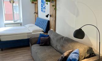 A modern room with a comfortable gray sofa and a bed in soft colors. Plants and decorative elements give the space a cozy atmosphere.