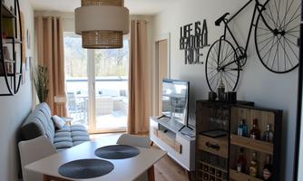 A modern living room with a gray sofa and a large window. A bicycle is hung on the wall and there is a dining area with a table and chairs.