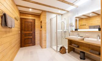 A modern bathroom with wood paneling. There is a shower, two sinks, and large windows for natural light.