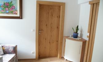 A bright room with a wooden door and a white cabinet. On the cabinet, there is a pot with a plant, and a picture hangs on the wall.