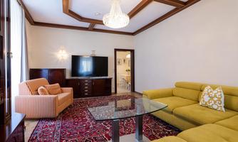 A cozy living room with a yellow sofa and a large rug. A television and a modern lamp are also available.