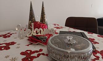 A festively decorated table with a "Welcome" sign, two hat tips, and an elegant box. The table is covered with a red floral patterned tablecloth.