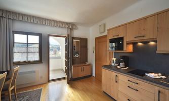 A modern kitchen with wooden cabinets and a dining table. Plenty of light enters the room through the window and the door.